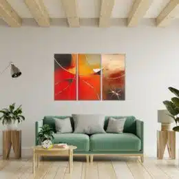 tableau triptyque abstrait rouge et beige au dessus d'un canapé moderne vert et gris dans un intérieur boisé.