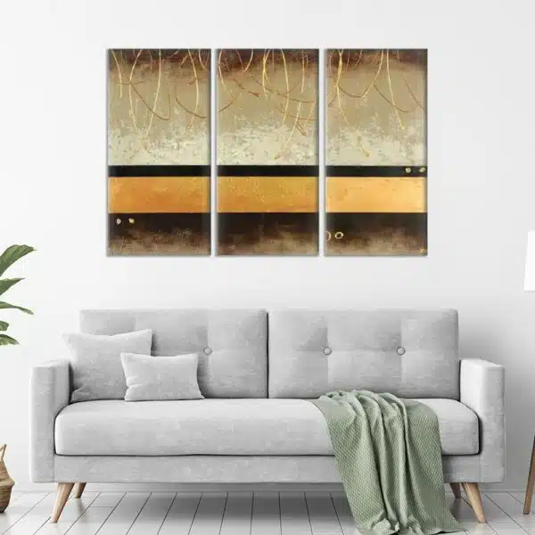 tableau triptyque marron or sur mur blanc au dessus d'un canapé gris avec une couverture verte sur le dessus.