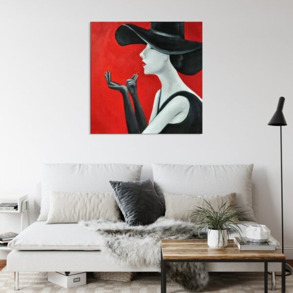 Tableau d'une femme avec un chapeau de profil faisant semblant de se mettre du rouge à lèvre, accroché au-dessus d'un canapé avec coussins noir, une table en bois et une lampe sur pied noir dans le coin droit
