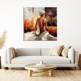 Tableau d'une femme de dos nue avec un bonnet et un drap autour de sa taille qui couvre ses jambes, avec des couleurs chaudes, marron, jaune, gris, orangé, accroché au-dessus d'un canapé beige avec 2 coussins beige foncé et une table basse en rotin
