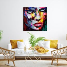 Tableau style pop art d'un visage d'une femme au regard poignant, accrcohé au-dessus d'un canapé blanc avec des coussins jaune, une table en verre avec une plante verte, 2 fauteuils en rotin