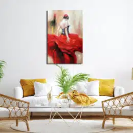 Tableau d'une danseuse de flamenco de dos avec une jupe à volant rouge et un bustier noir, accroché au-dessus d'un canapé blanc avec des coussins jaune, une table basse en verre avec une plante, 2 fauteuils en rotin bois