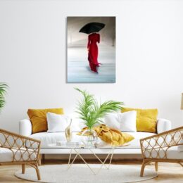 Tableau d'une femme en robe rouge de dos avec un parapluie noir, accroché au-dessus d'un canapé blanc avec des coussins jaune, une table basse en verre avec une plante verte posée dessus, 2 fauteuils en rotin