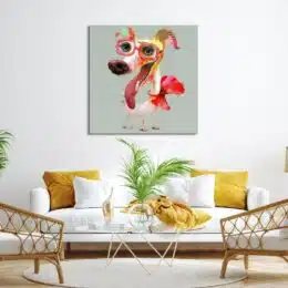 Tableau petit chien rose pop art avec des lunettes et des yeux bleus, un petit nœud rouge autour du cou, accroché au-dessus d'un canapé blanc avec des coussins jaune devant une table basse en verre avec une plante verte, 2 fauteuils en rotin bois qui forme un salon