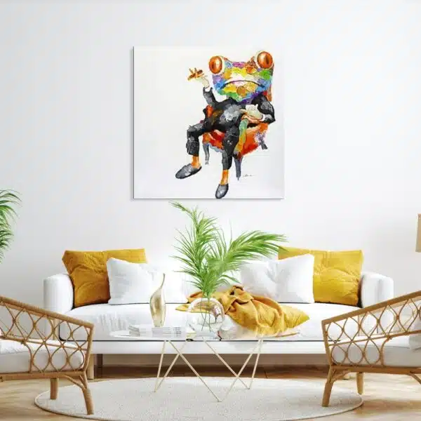 Tableau style pop art d'une grenouille assise dans un fauteuil orange avec un costume noir et un cigare, accroché au-dessus d'un canapé blanc avec des coussins jaune, une table en verre avec une plante verte et 2 fauteuils en rotin bois