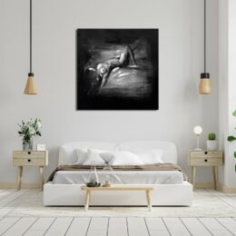 Tableau noir et blanc d'une femme étendue les bras derrière la tête, la jambe droite pliée , accroché au-dessus d'un lit avec 2 suspensions lumières au-dessus de 2 chevets en bois patine blanc muni de 2 tiroirs chacun et d'une plante posée sur celle de gauche et une lampe et un cactus sur la droite, un banc au bout du lit avec un petit voilier