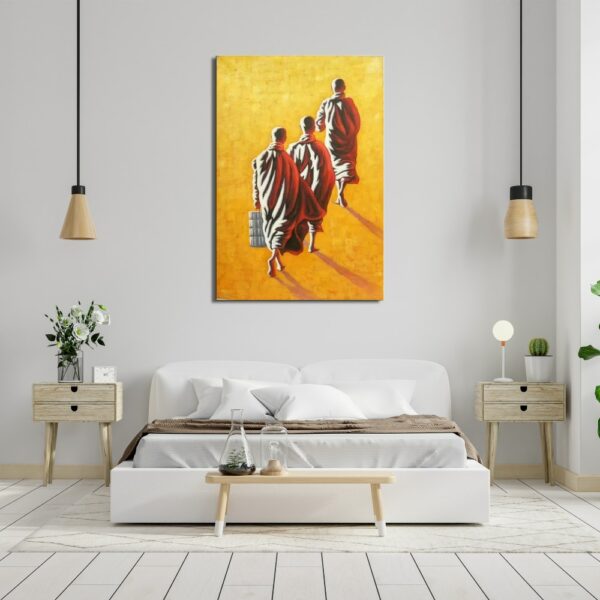 Tableau sur fond jaune sable avec 3 moines marchant de dos en robe rouge et un sac dans la main gauche , accroché au-dessus d'un lit avec un banc au bout, 2 susepnsions de lumière au-dessus des 2 tables de chevet en bois avec tiroirs, une plante à gauche et une lampe à droite