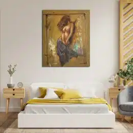 Tableau aux couleurs chaudes d'une femme nue avec un drap qui couvre le bas de ses jambes, la tête tournée et ses cheveux qui couvrent son visage, accroché au-dessus d'un lit avec un plaid jaune et 2 tables de chevet en bois avec un fauteuil gris sur la droite