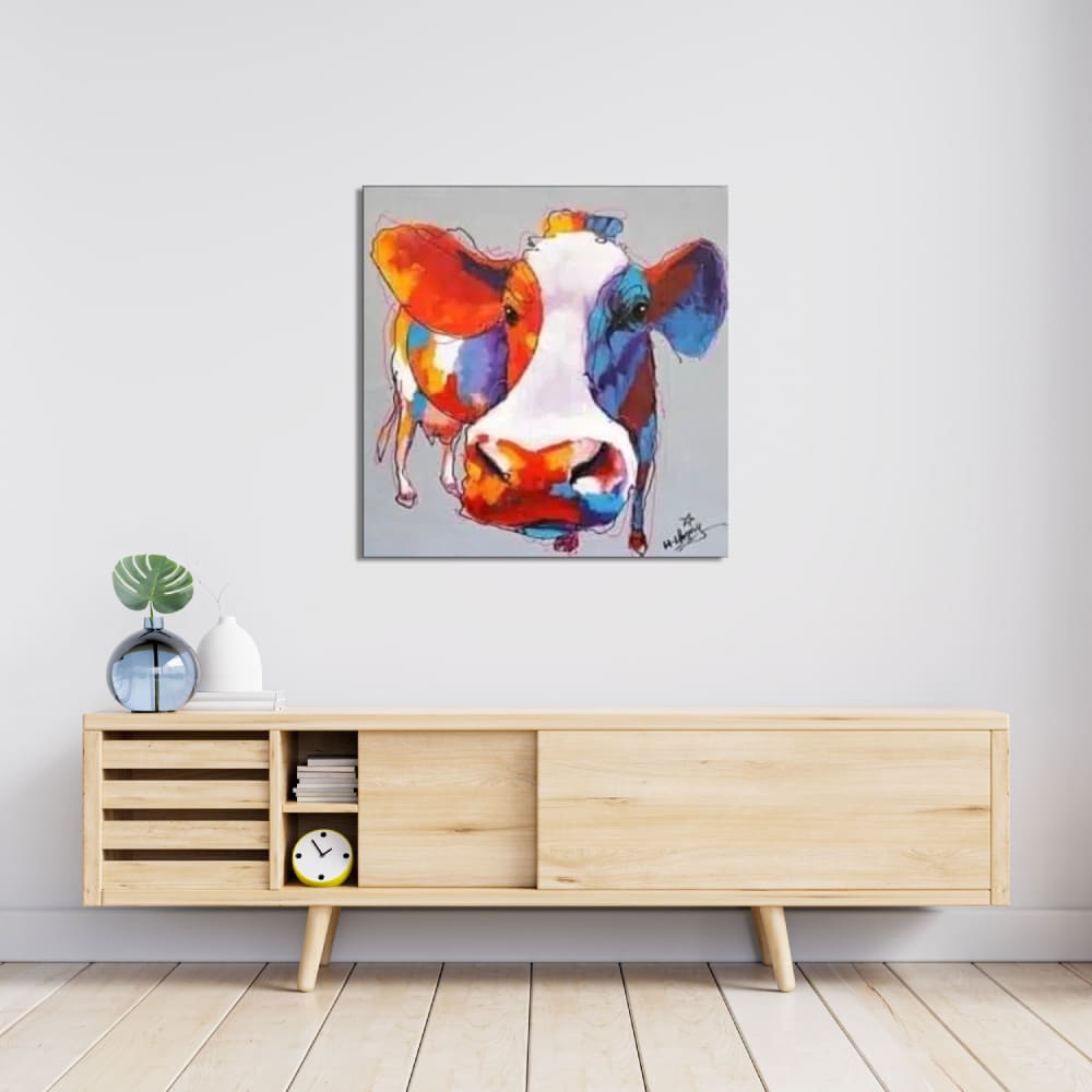 Tableau pop art d'une vache aux couleurs bleu et orange , accrcohé au-dessus d'un long meuble en bois clair avec 2 portes coulissantes, un vase bleu transparent sur la gauche
