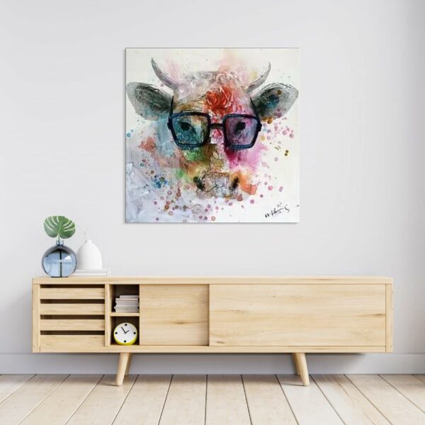 Tableau style pop art d'une vache à lunette avec des couleurs multicolore, accroché au-dessus d'un meuble en bois avec 2 portes coulissantes, un vase bleu transparent sur la gauche