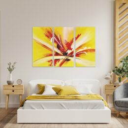tableau triptyque abstrait rouge et jaune sur un mur blanc dans une chambre au dessus d'un lit au draps blancs et coussins jaune.