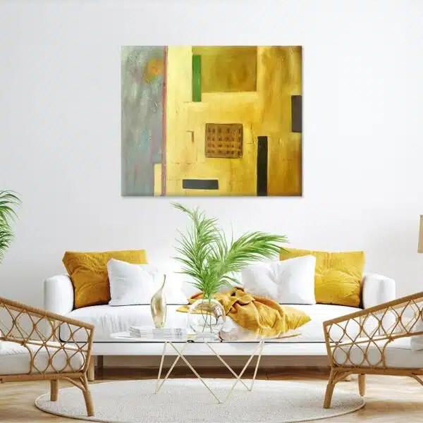 tableau abstrait jeune et gris posé sur un mur blanc au dessus d'un canapé blanc aux coussins jaunes.