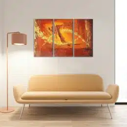 Tableau abstrait triptyque orange sur un mur blanc au dessus d'un petit canapé jaune moderne et à coté d'une lampe métallisée.