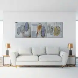 tableau triptyique abstrait gris au dessus d'un grand canapé gris entouré de lampes dorées.