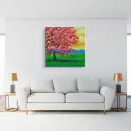 Tableau arbre en fleurs dans un champ, accroché sur un mur dans un salon avec un canapé et une table