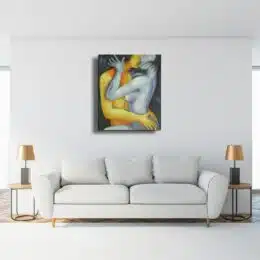 Tableau d'un couple s'embrassant la femme à droite dans les couleurs bleue, gris et l'homme à gauche dans les couleurs jaune, orangé accroché au-dessus d'un canapé gris avec 2 table d'appoint et 2 lampes au abat-jour cuivre