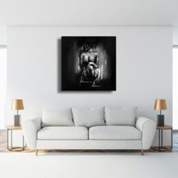 Tableau noir et blanc d'une femme nue accroupie, accroché au-dessus d'un canapé gris et 2 tables d'appoint avec 2 lampes chics dans les tons cuivrés