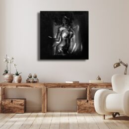 Tableau noir et blanc d'une femme nue debout, accroché au-dessus d'une table en bois foncé avec des caisses de rangement en dessous et un fauteuil blanc