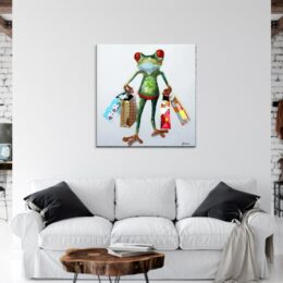 Tableau d'une grenouille revenant du shopping avec des sacs des 2 côtés, accroché au-dessus d"un canapé bla,c avec 2 coussins noirs et une table basse en bois
