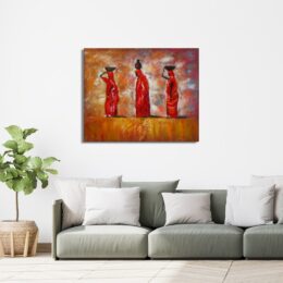 Tableau de 3 femmes africaines portant des corbeilles sur la tête dans un décor désert aux tons oranges, rouges, accroché au-dessus d'un canapé vert avec des coussins beige, une plante verte dans un pot en terre sur la gauche
